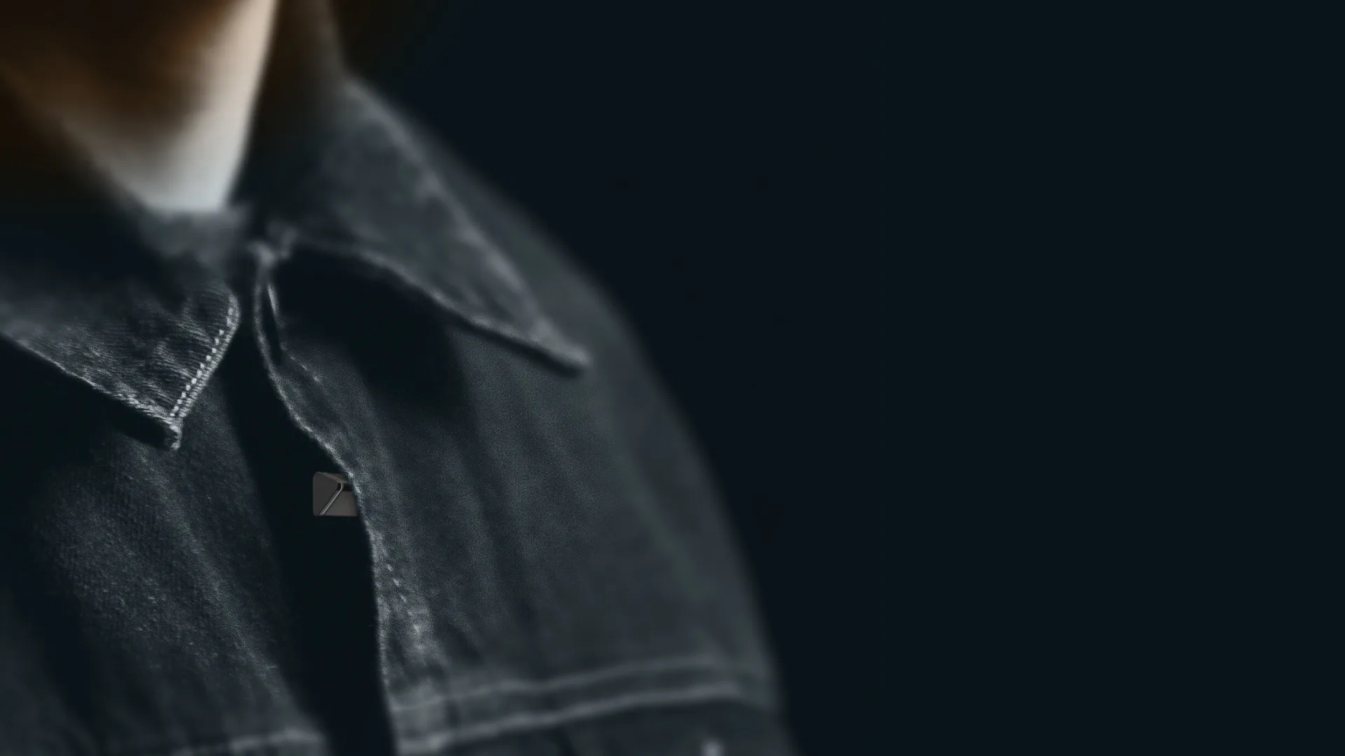A small Fountain Pen on the lapel of a denim jacket against a dark backdrop.